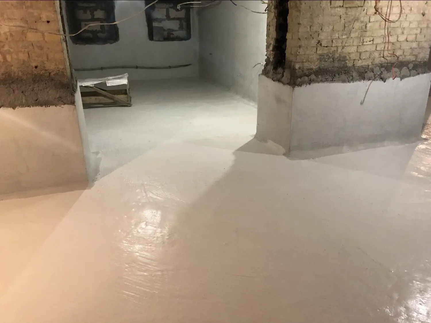 Нанесений гідроізоляційний шар білого кольору на підлогу та частину стін підвалу