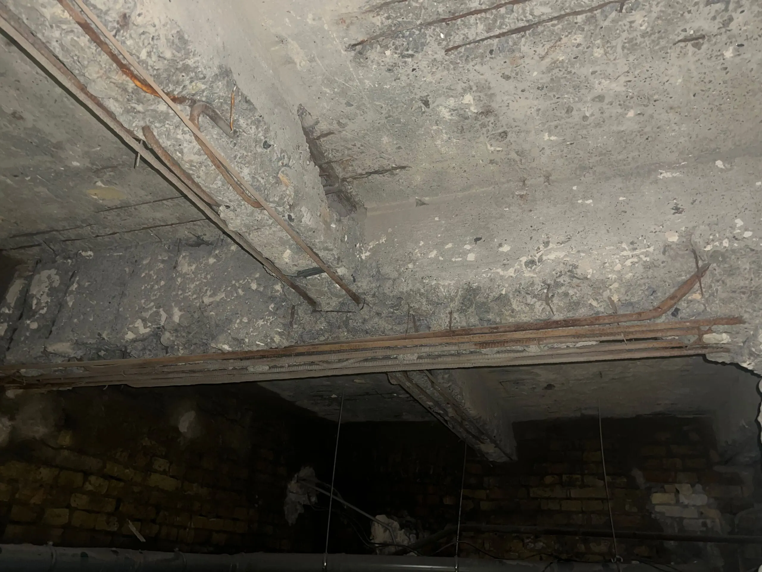 Фото пошкодженого бетону на стелі підвального приміщення з видимою оголеною арматурою